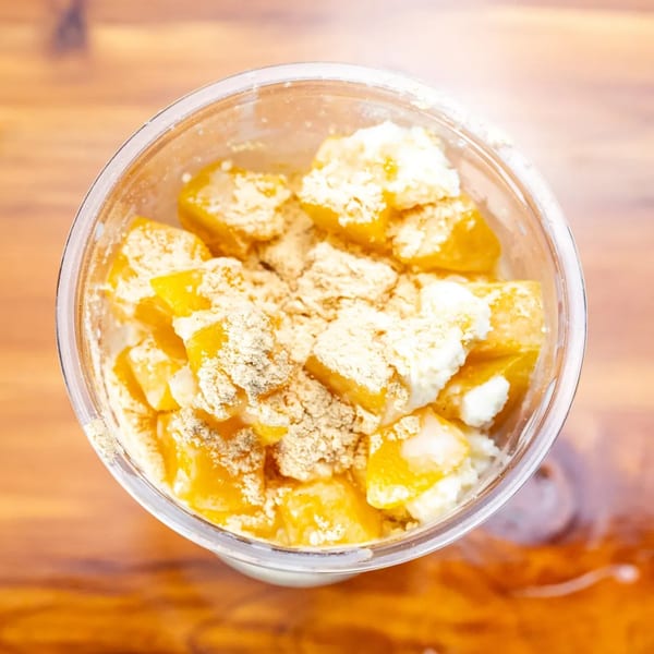 Overhead view of a clear cup filled with diced mango, white cream, and a brown powder.