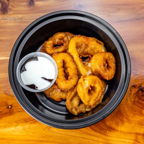 Golden-brown fried calamari rings and tentacles with a side of white dipping sauce in a black bowl.