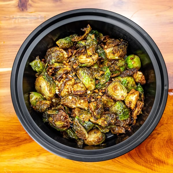 Crispy roasted Brussels sprouts with garlic and seasoning in a black bowl on a wooden table.