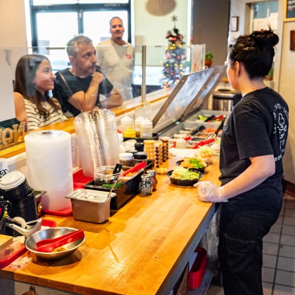 Pokefit employee preparing food at a counter for customers, with a Christmas tree in the background.