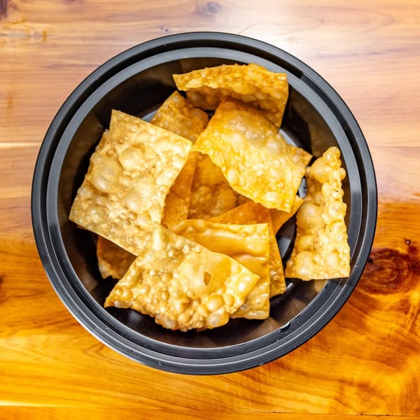 Crispy golden wonton chips in a black bowl on a wooden table at Pokefit.