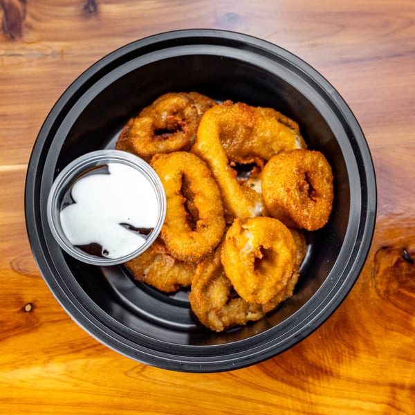 A black bowl filled with golden-brown onion rings and a small cup of white dipping sauce.
