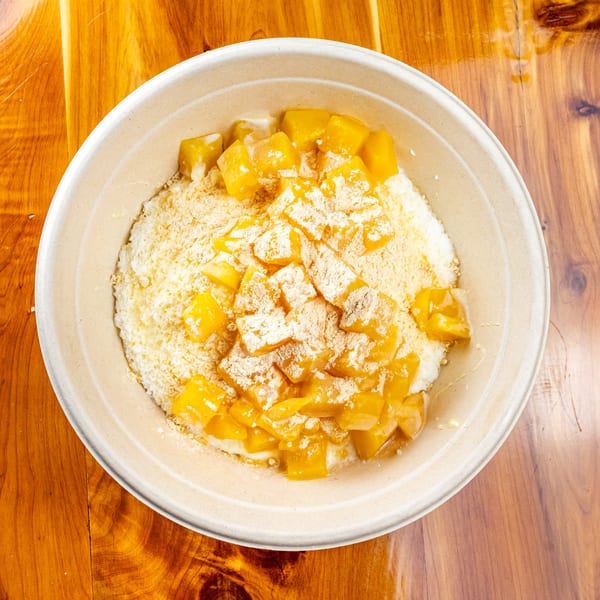 A close-up of a Pokefit mango dessert with shaved ice and powdered topping in a bowl.