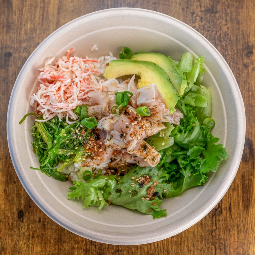 A Pokefit poke bowl with crab, avocado, seaweed, and greens on a wooden table.