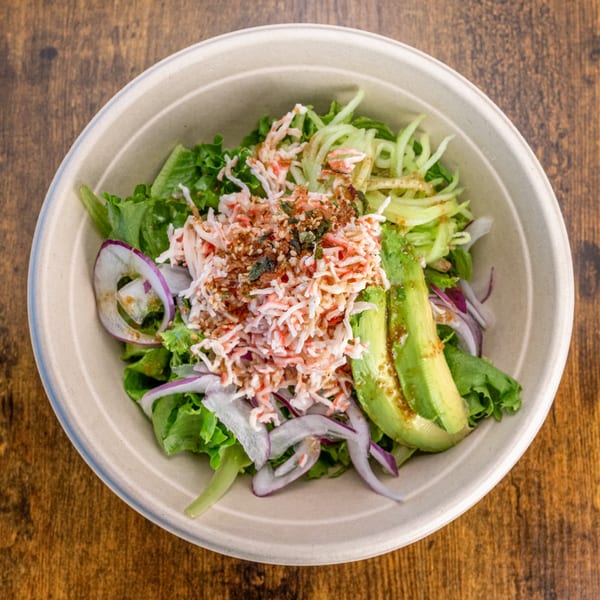 Pokefit's Asian-fusion salad with crab, avocado, red onion, and greens in a bowl.