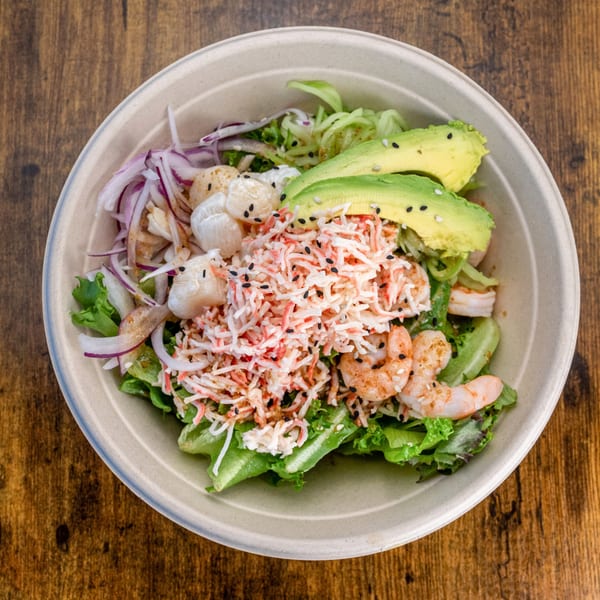 Pokefit poke bowl with shrimp, crab, scallops, avocado, and red onions over greens.