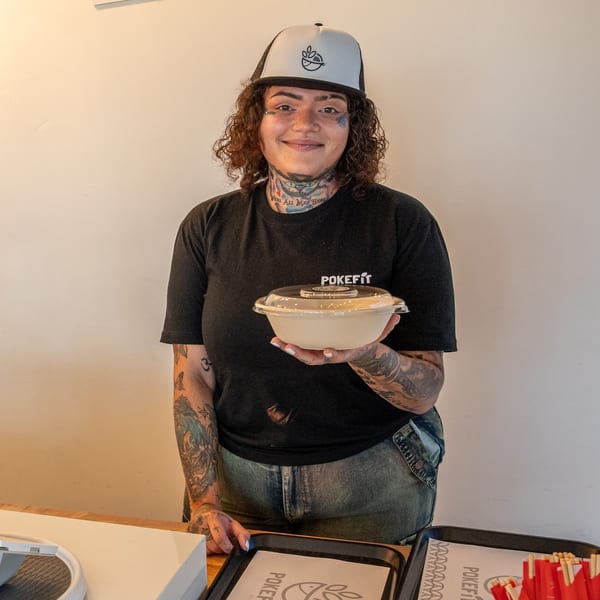 A smiling Pokefit employee in a branded hat and shirt holds a poke bowl.